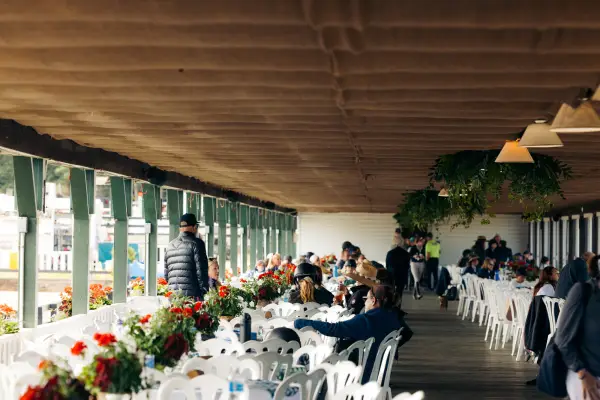 A few people sit at rows of white round tables and chairs in pavilion building