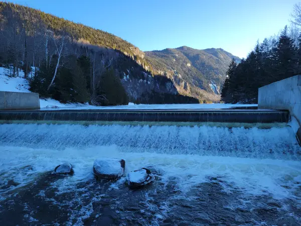 A long dam with water spilling over the top in the winter