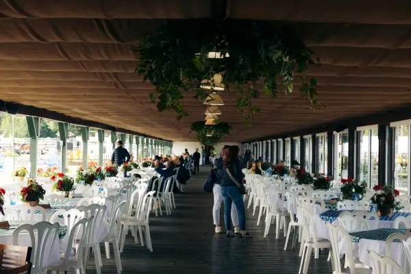 Two rows of round white tables and chairs line either side of pavilion building with some people standing in aisle