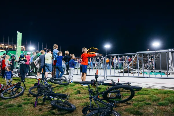 Bikes litter the lawn and children stand against event fencing watching BMX stunt show on Olympic Oval