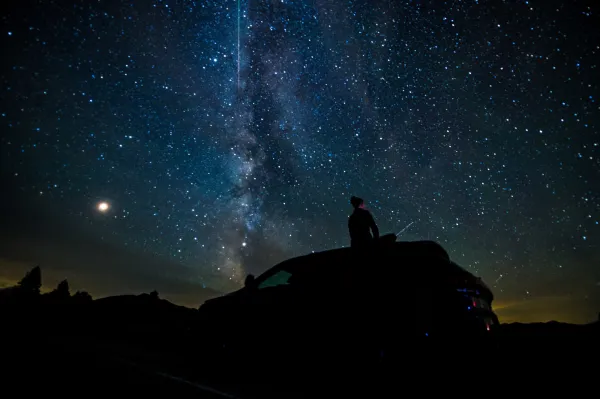 Person sits on the top of a vehicle viewing the stars under the Adiroddack night sky.