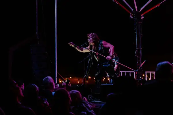 Singer leans out over stage singing in dark outdoor setting with crowd in front of the stage