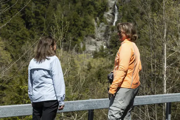 Two woman standing on the side of the road in front of a waterfall