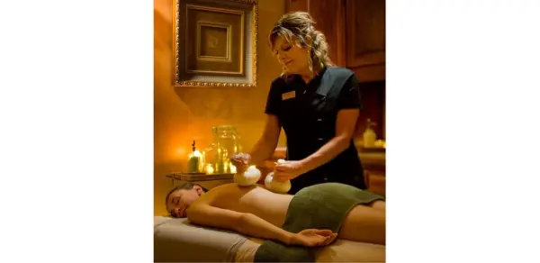 A massuse administers a thai herbal massage to a relaxed woman in a comfortable private room