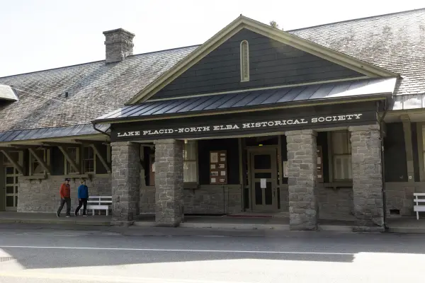 Two people walk on covered walkway up to the doors of the Lake Placid–North Elba Historical Society & Museum