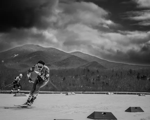 Black and white image of two men cross-country skiing on a competition trail with mountains in the background