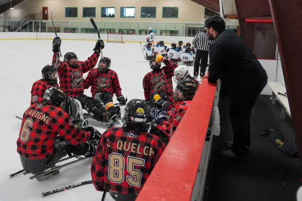 A sled hockey team in plaid jerseys celebrates on the ice during a game, showcasing camaraderie and excitement.