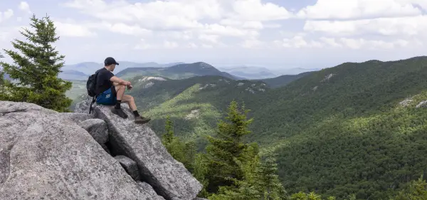 A hiker sits on a large rock on a summit