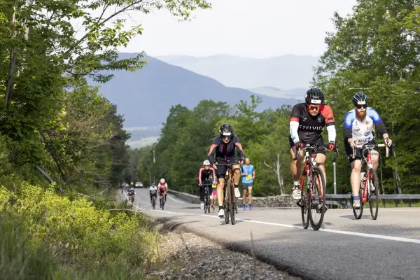 A group of cyclists going up a road with mountains behind them