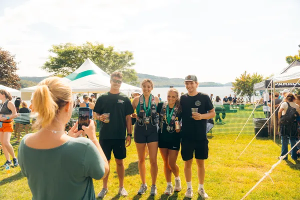 A woman takes a photo on her phone of four friends posing together with drinks and finisher medals.