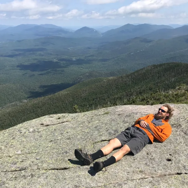 A hiking guide lays on a large rock overlooking a valley surrounded by mountains.