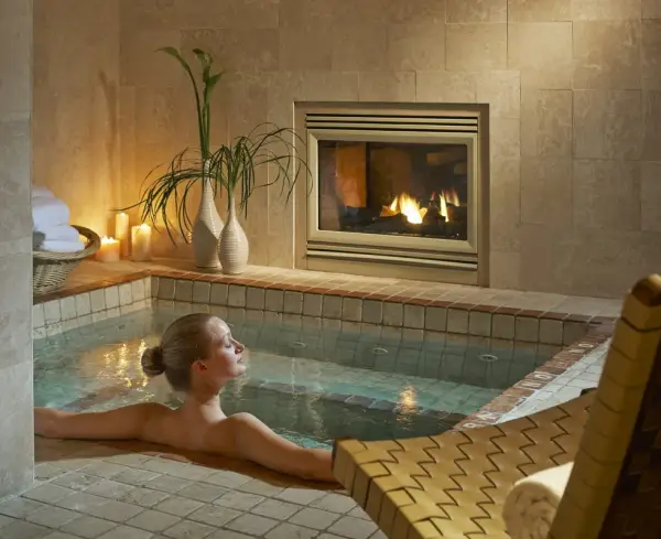 A woman relaxes in a private pool with fireplace and candles surrounding