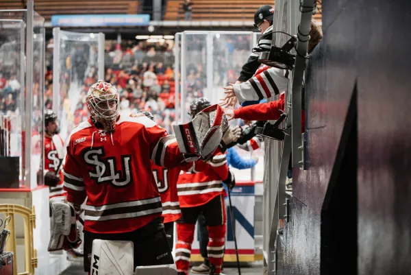 Members of the St Lawrence University hockey team give high fives and fist bumps to hands reaching over partition as they leave the ice