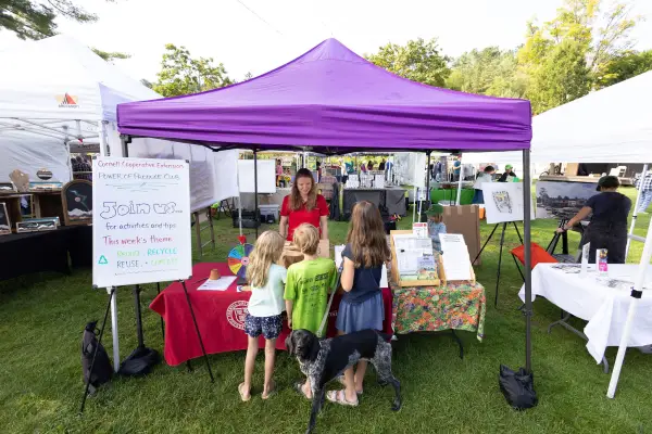 A purple tent at an outdoor event with a table displaying information about the Cornell Cooperative Extension's Power of Produce Club.