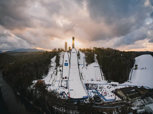 Straight on aerial shot of Lake Placid Ski Jumps in winter with sun setting behind the jump towers