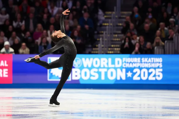Male figure skater in black long sleeve and long pant spandex costume performs back bending move on ice