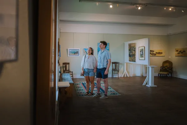 Man and woman stand holding hands in open concept art gallery in natural light looking at art wearing summer clothes