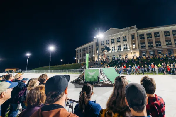 Stunt rider flips in mid-air over temporary jump on the track of the Olympic Oval at night as crowd looks on