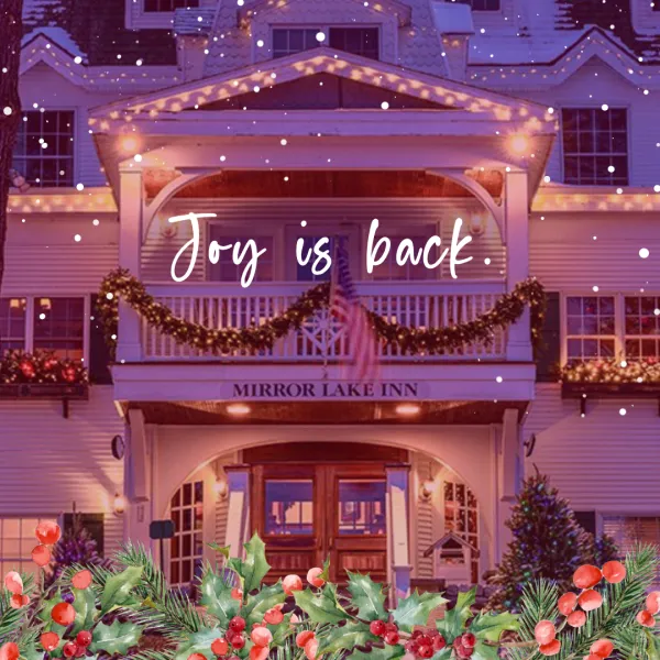 Festive inn entrance with twinkling lights and garlands. Snow falls gently. The text "Joy is back" overlays. Foreground: holly and berries. Cozy and cheerful.