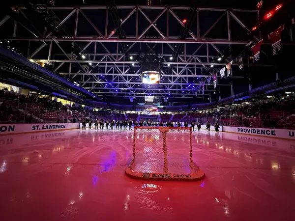 On-ice photo of hockey players lined up center ice with red lights illuminating the ice in the 1980 Herb Brooks Arena in Lake Placid