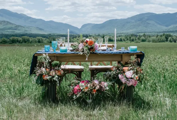 The Sweetheart table adorned with flowers, candles and blue glass in a meadow with the high peaks mountains in the background