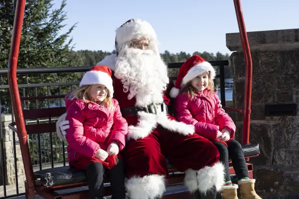A couple of children having their picture taken while sitting next to Santa.