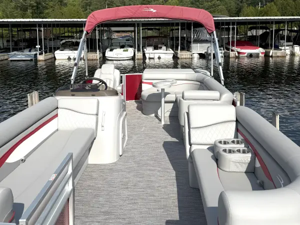 A red and white pontoon boat is docked at the marina with other boats in the covered slips behind