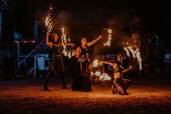 Trio of fire dancers seen with lighted torches posing in dark outdoor venue