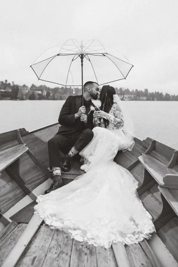 Black and white photo of the bride and groom kissing under an umbrella in the rain