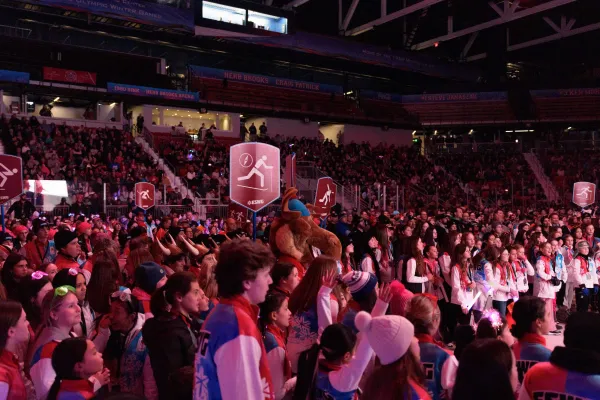 A large crowd fills an indoor arena, watching the Empire State Winter Games Opening Ceremony.  The atmosphere is vibrant and energetic.