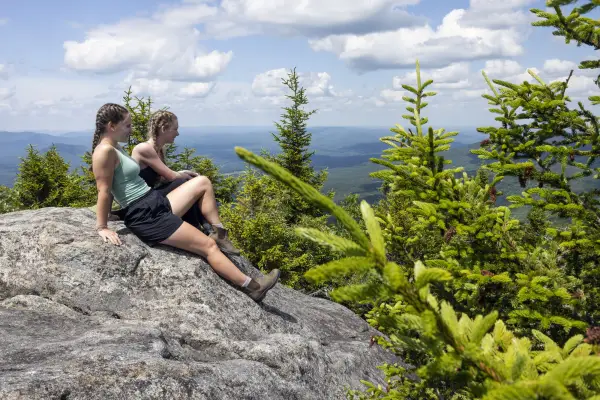Two young women sit on a rocky summit.