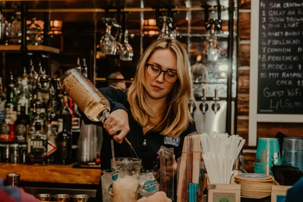 A smiling bar tender makes a cocktail with the full bar at Big Zs.  Photo Credit to A. Kelly.