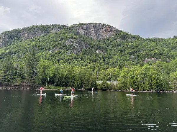 Five people are seen paddling on NRS paddle boards during a paddle clinic on Chapel Pond in the Adirondacks