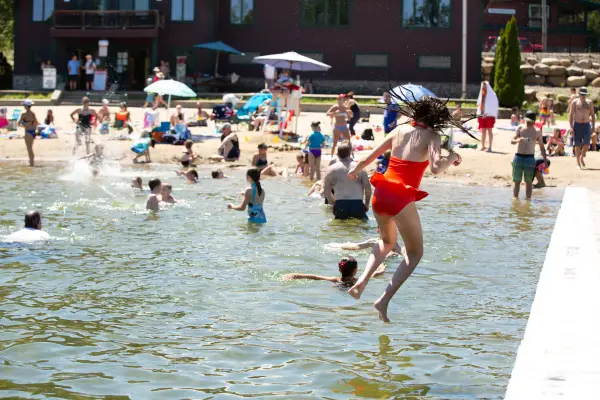 People swimming at the beach and jumping off a dock.