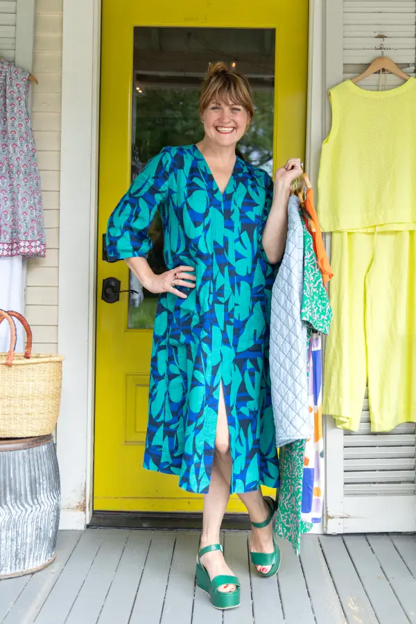 A happy lady in her blue dress stands holding her clothing haul.