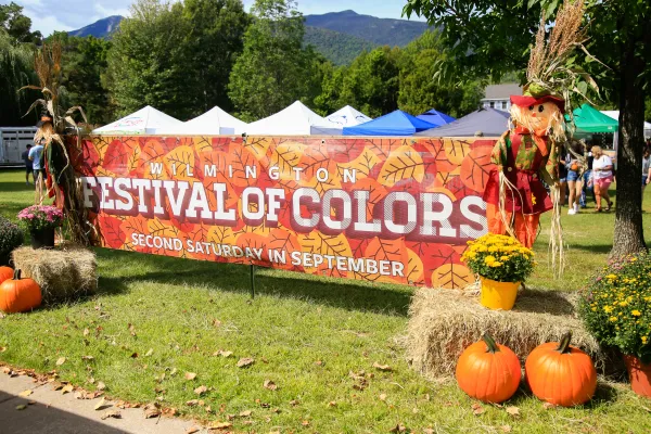 Large horizontal Festival of Colors banner in front of event bookended by hay bales, mums, pumpkins, and scarecrows