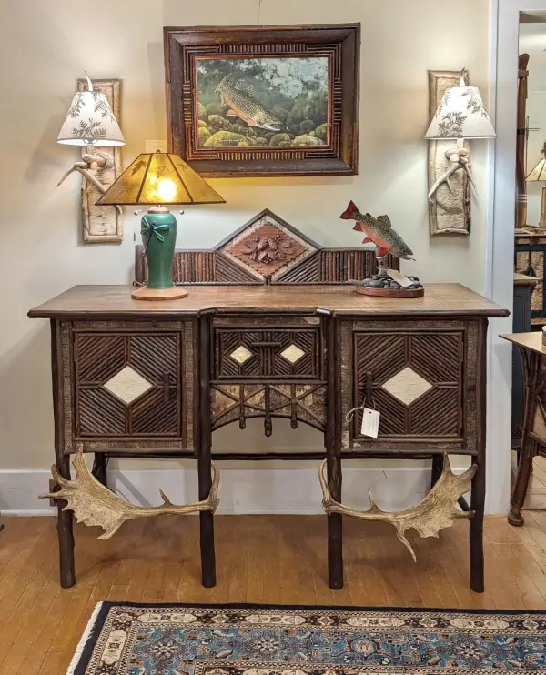 A rustic buffet table decorated with twig work and antlers, and a painting of salmon among a rocky stream bed in a matching twig frame.