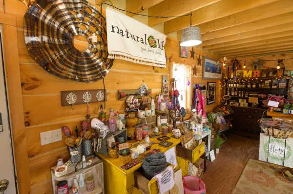 Colorful decor items, mugs, water bottles and kitchen utensils sit atop a yellow dresser in front of knotty pine walls