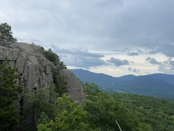 Mountain background while person climbs a shear cliff face in the forground