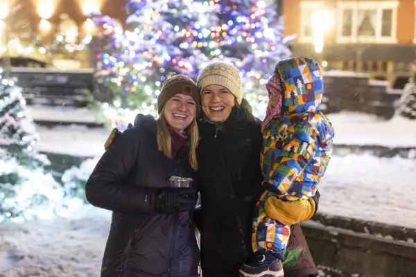 A group of people having posing for a picture in front of the Christmas tree out in the park.