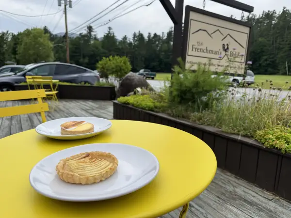 Two pastries sit on white plates on the yellow bistro tables on the wooden front deck of The Frenchman's Bakery.