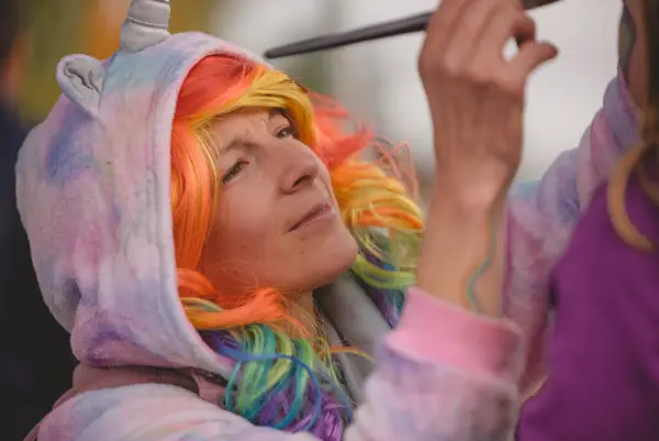 Woman with colorful hair paints a childs face at the fall festival.