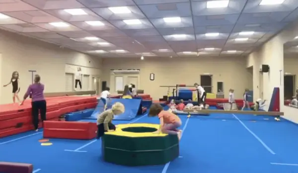 Room full of gymnastic mats and equipment and kids of varying ages practicing tumbling skills