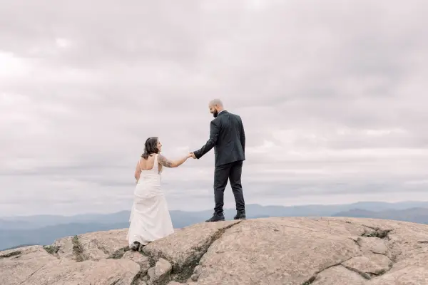 Bride and groom laugh atop a rocky knoll 