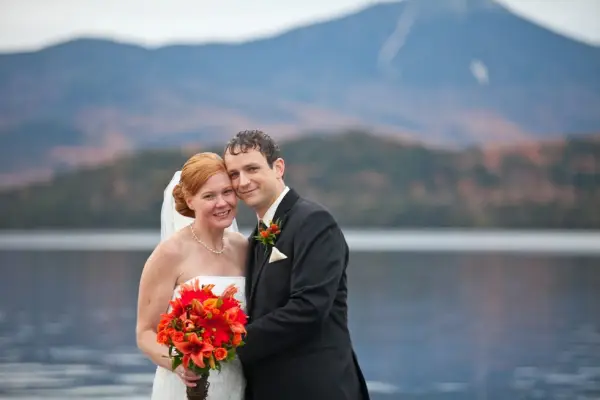 A happy couple smiles into the camera with the Mirror Lake and fall foliage covered mountains in the background