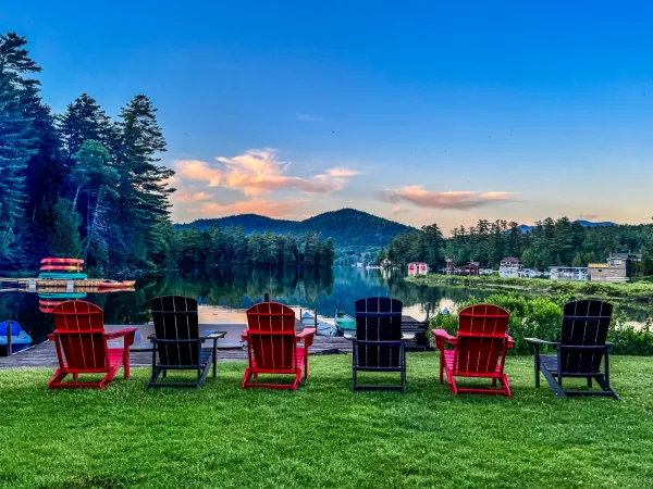 Red and green adirondack chairs by the mirror of the lake and mountains in the distance at Wildwood on the Lake.