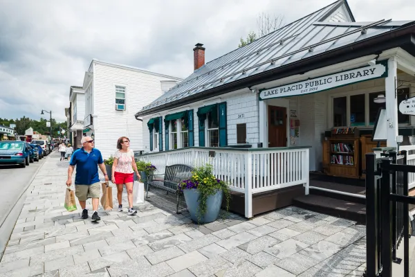 Senior couple carrying shopping bags walk past Lake Placid Public Library in summer