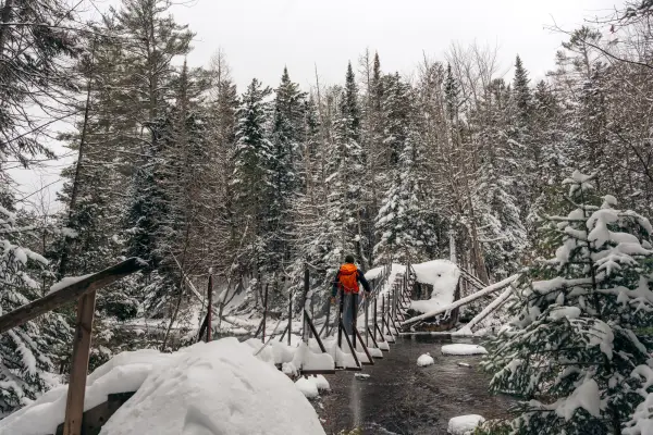 A snowshoer walks across a metal bridge