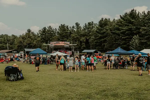 Music festival crowd seen in field with pop-up tents, some people seated in lawn chairs, and some people standing