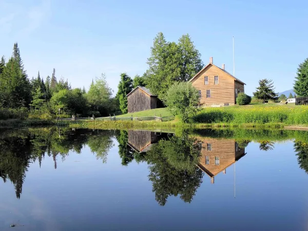 John Brown's house at John Brown Farm seen over and reflecting in a placid pond in summertime
